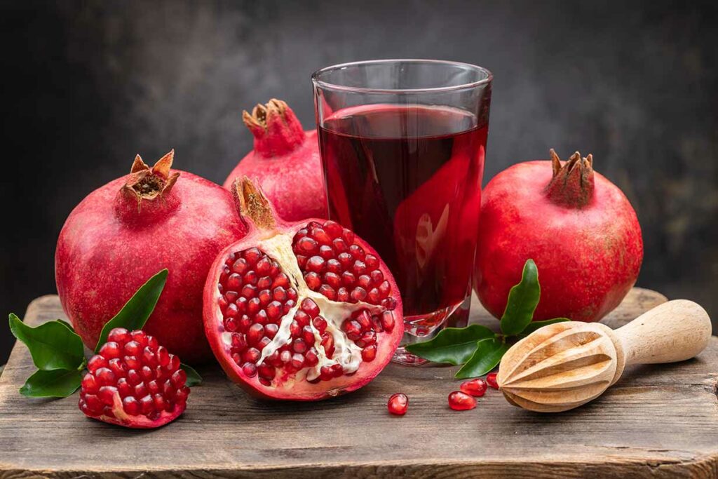 Whole and Half Pomegranates Showing Seeds, Next To Pomegranate Juice.