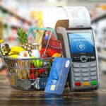 A Shopping Basket Filled With Foods Next To a Payment Machine Displaying Cost (Food Budgeting Theme).