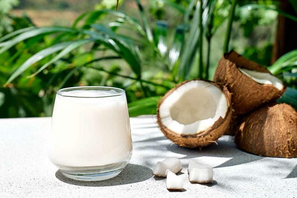 Coconut Milk In a Glass Next To Opened Coconuts.