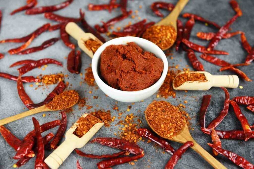 Cayenne Pepper Powder In a Bowl Surrounded By Dried Cayenne Peppers.