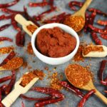 Cayenne Pepper Powder In a Bowl Surrounded By Dried Cayenne Peppers.