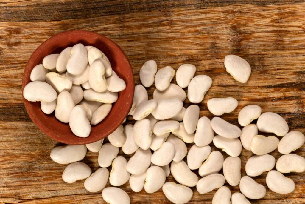 Raw lima beans in a bowl and spilling onto a wooden surface.