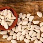 Raw lima beans in a bowl and spilling onto a wooden surface.