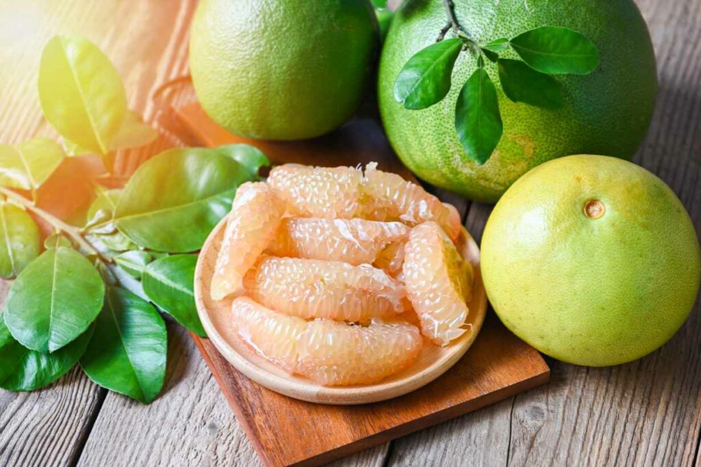 Whole Pomelo Fruit In Peel Next To Unpeeled Pomelo Slices.