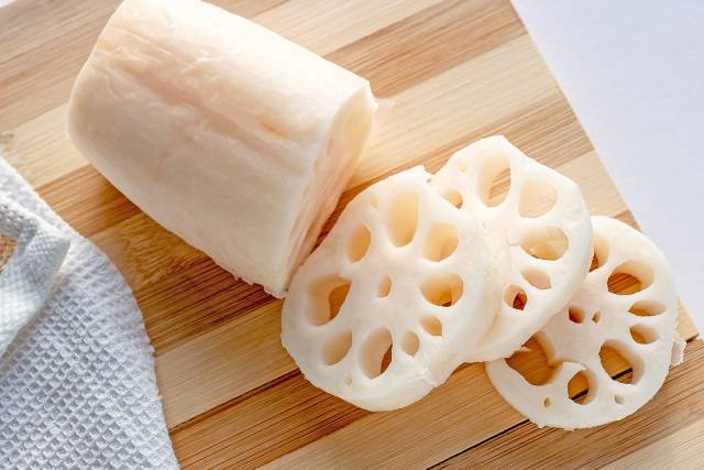 Sliced lotus root pieces on a wooden cutting board.