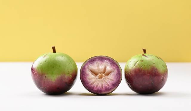 Two whole purple star apples and one cut in half showing inner flesh.