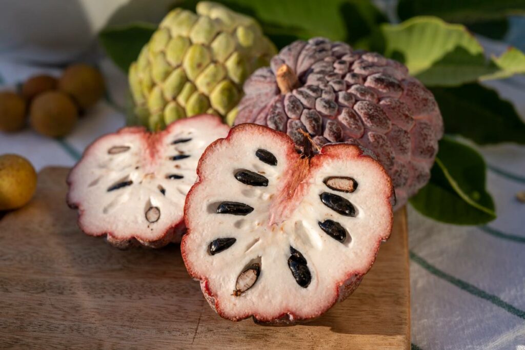 A whole cherimoya fruit next to two halves showing the fruit's flesh.