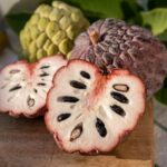 A whole cherimoya fruit next to two halves showing the fruit's flesh.