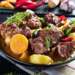 A goat meat stew dish in a black bowl.