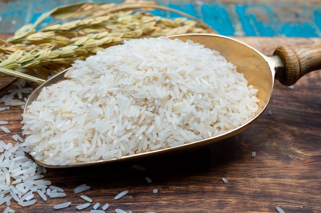 Dried basmati rice in a scoop on a wooden table.