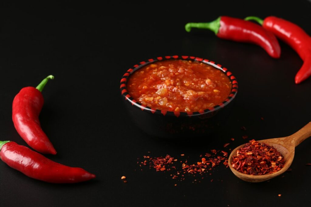 Small bowl of harissa paste next to red chili peppers.