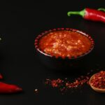 Small bowl of harissa paste next to red chili peppers.