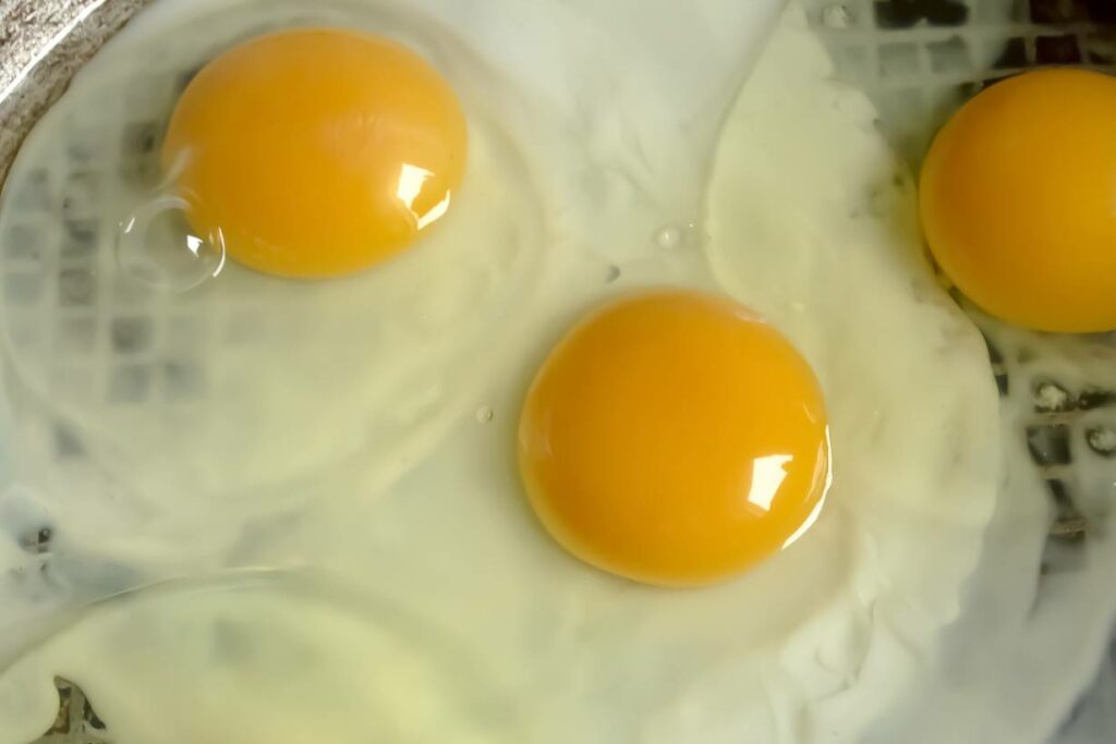 Three eggs in a pan cooking.