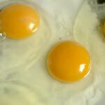 Three eggs in a pan cooking.