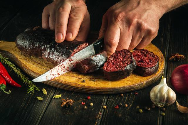 A chef cutting blood sausage into pieces with a knife.