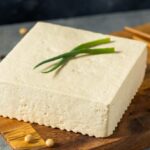 A block of extra firm tofu on a wooden board.