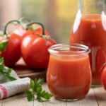 A glass of tomato juice next to whole red tomatoes.