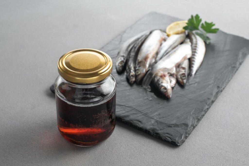 A glass jar of fish sauce next to several small fish.