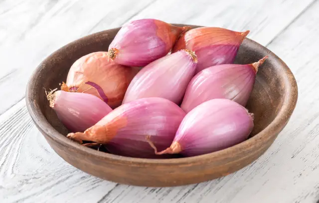 A wooden bowl containing eight shallots.