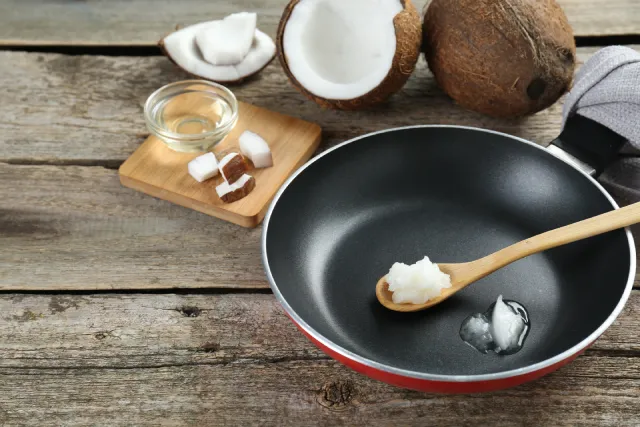 Coconut oil on a wooden spoon in a frying pan.