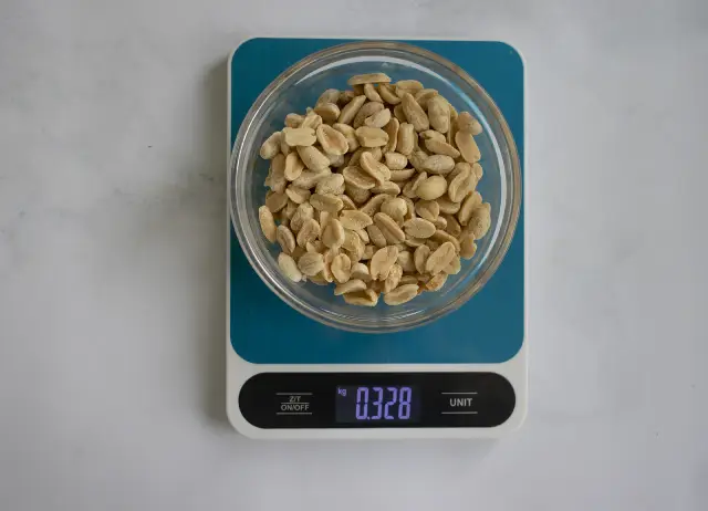 Digital kitchen scales with a bowl on top containing peanuts.