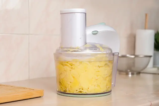 A food processor containing thinly-sliced potatoes.