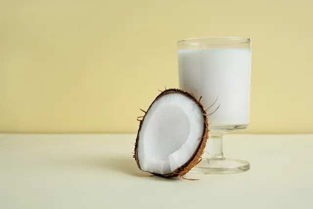 A glass of coconut milk next to half a coconut.