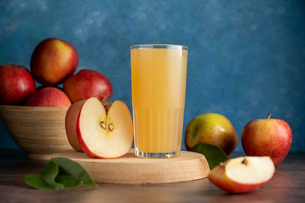 A glass of cloudy apple juice surrounded by fresh apples.