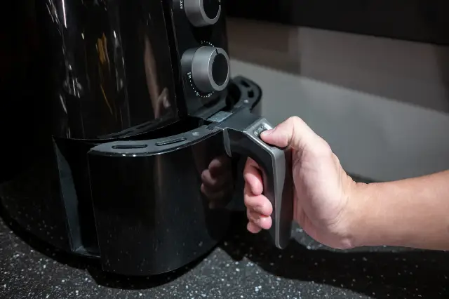 A man holding the tray handle of an air fryer.