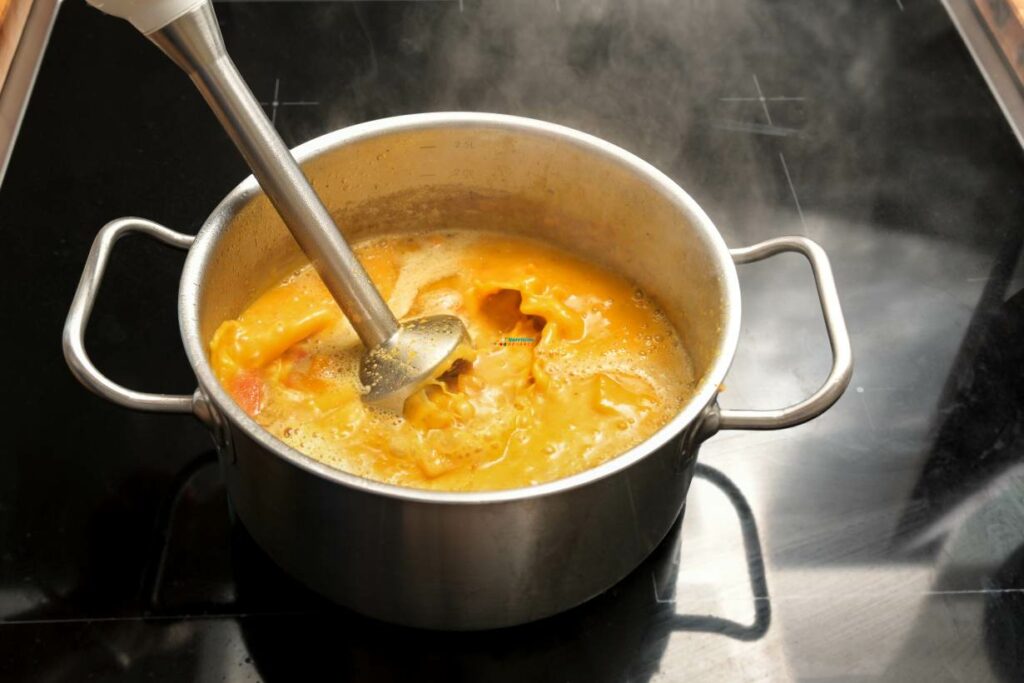 Pureeing cooked food in a cooking pot with an immersion blender.