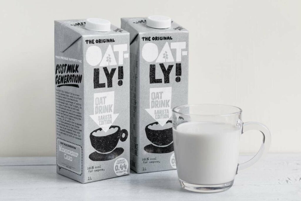 A carton of oat milk next to a glass of oat milk.