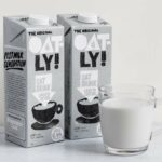 A carton of oat milk next to a glass of oat milk.