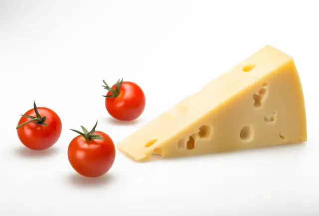 A wedge of Emmental cheese next to some cherry tomatoes.