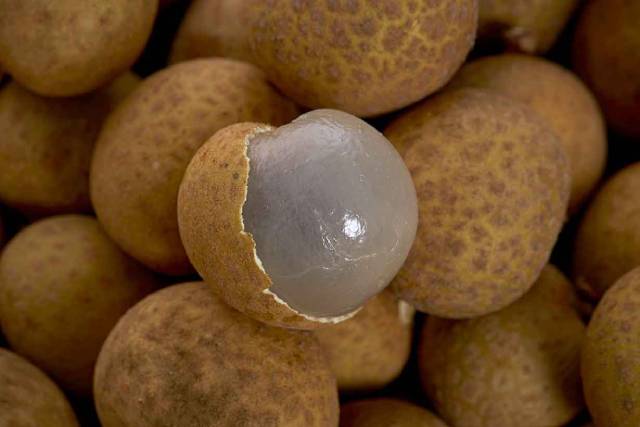A pile of whole longan fruits with one peeled.