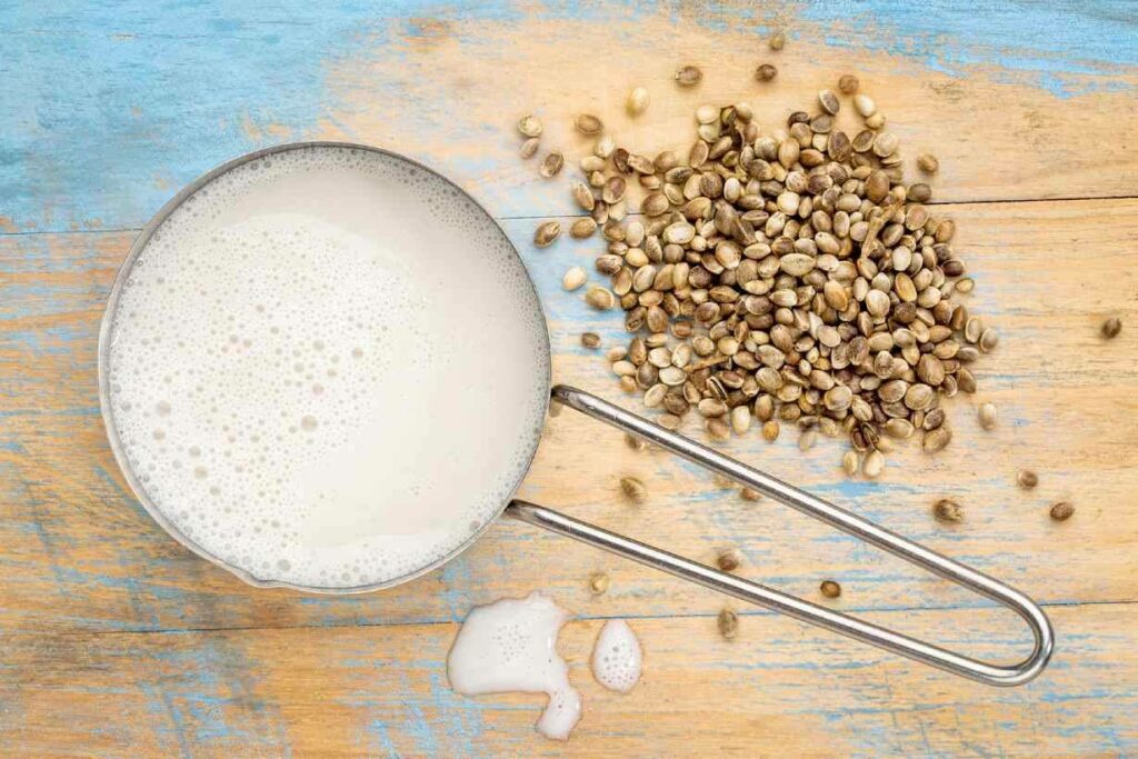 Hemp milk in a cup next to hemp seeds on a wooden surface.