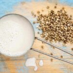 Hemp milk in a cup next to hemp seeds on a wooden surface.