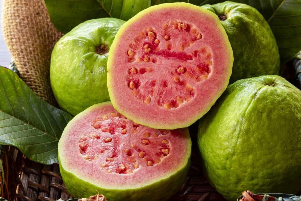 Whole guava fruit and a guava cut in half showing its red flesh.