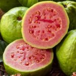 Whole guava fruit and a guava cut in half showing its red flesh.