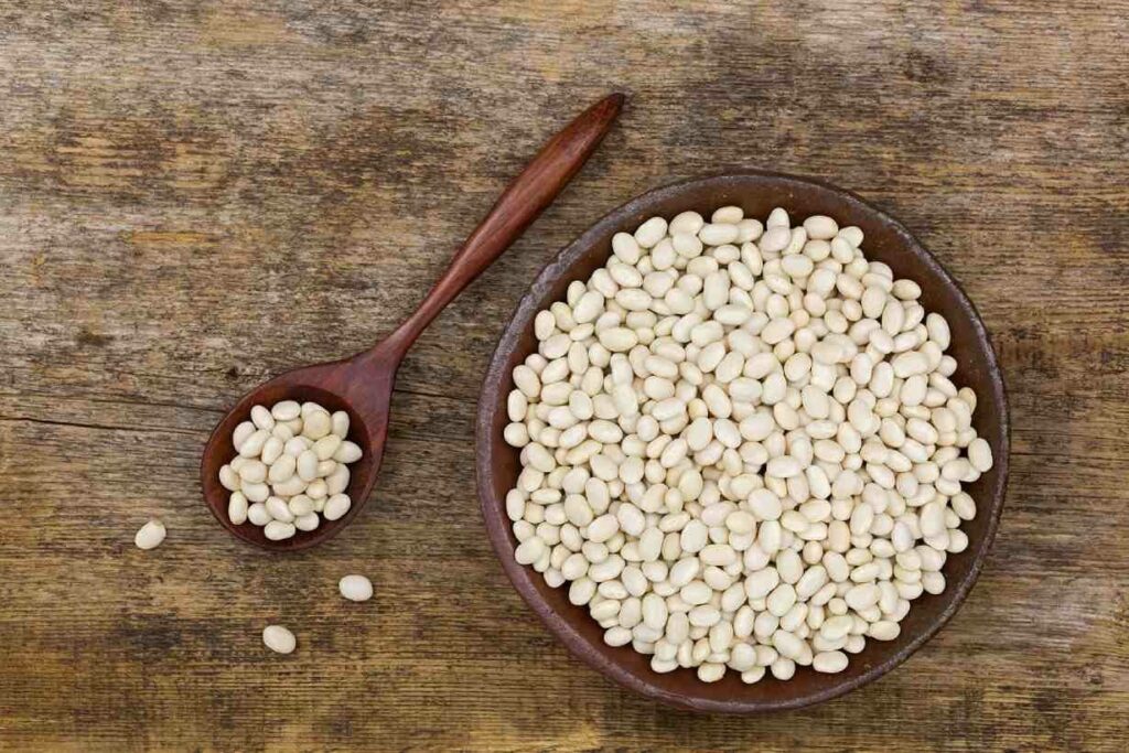 Navy beans in a wooden bowl on a wooden surface.