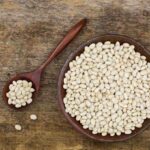 Navy beans in a wooden bowl on a wooden surface.