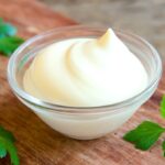 Small glass container of mayonnaise on a wooden surface.