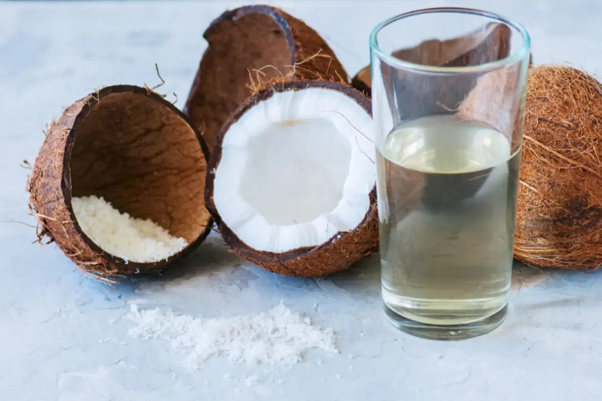 Coconut water in a glass next to two coconut halves.