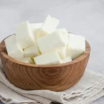 Large pieces of paneer cheese in a wooden bowl.