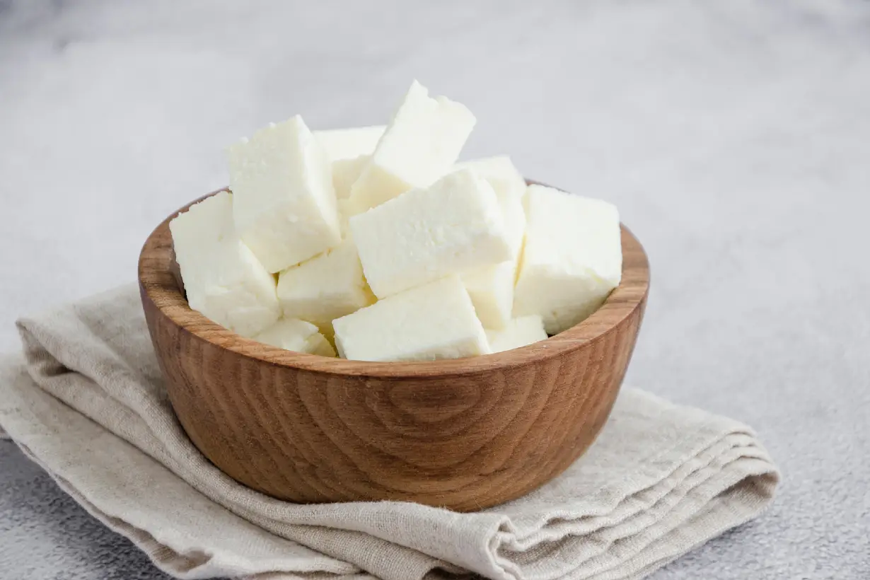 Large pieces of paneer cheese in a wooden bowl.