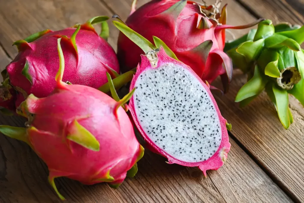 Three whole dragon fruit and one cut in half showing its flesh.