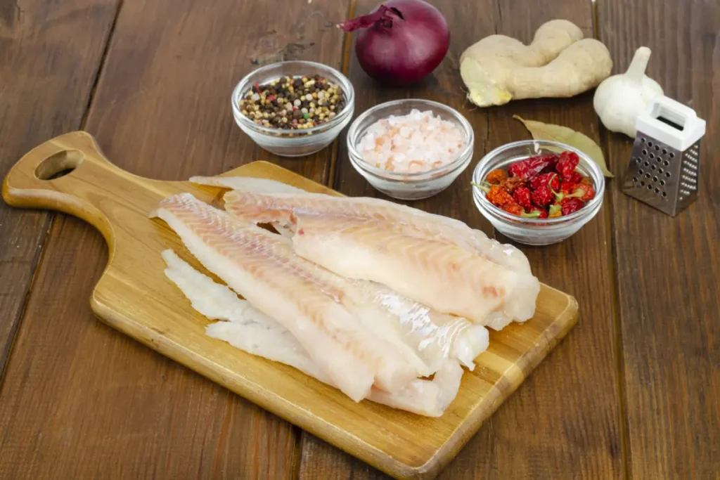 Several raw fillets of pollock on a wooden board.