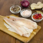 Several raw fillets of pollock on a wooden board.