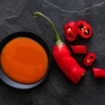 Hot sauce in a small black dish next to a chopped red chilli pepper.