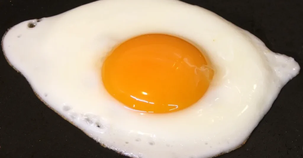 Fried egg on a black background, showing the egg white and yolk.