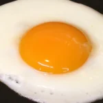 Fried egg on a black background, showing the egg white and yolk.